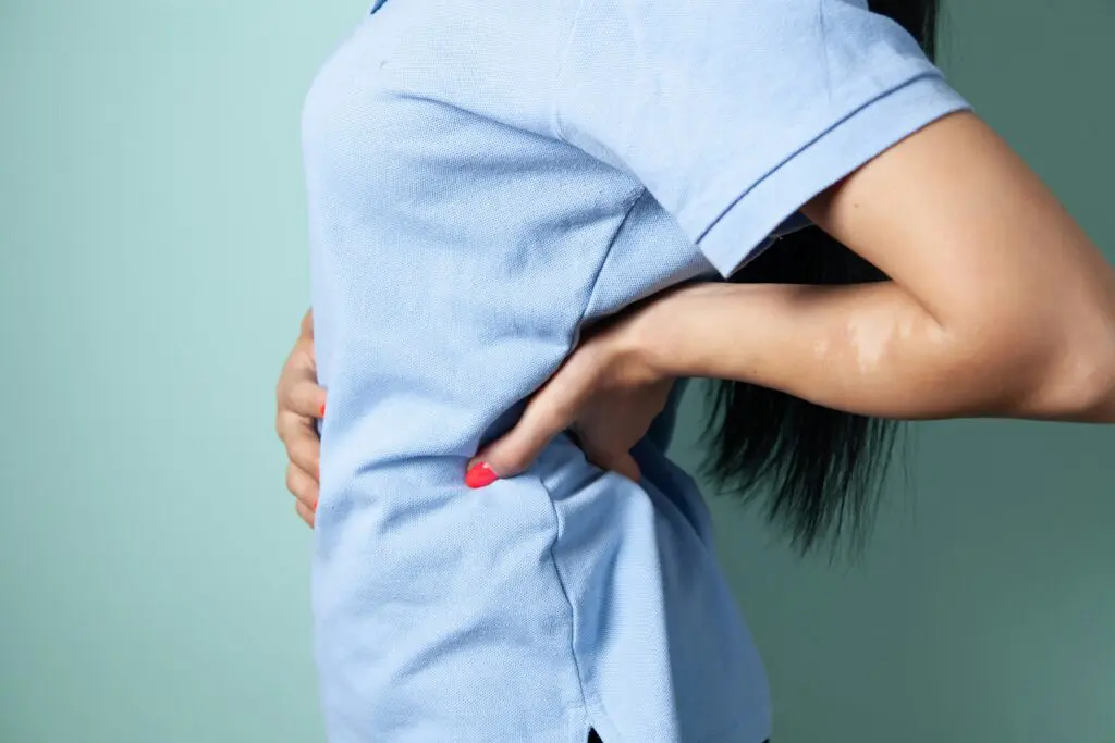 Neck-down close-up image of an employee holding her back due to injury at work.